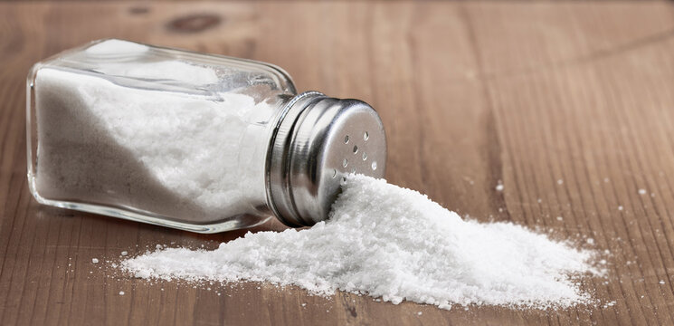 Salt glass jar and pile of spilled salt on a wooden table