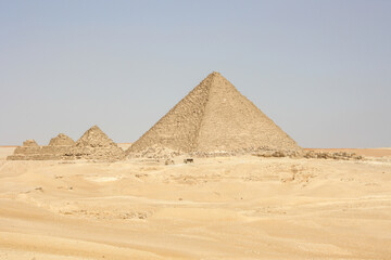 Fototapeta na wymiar pirámide con otras pirámides pequeñas a su lado en medio del desierto un día despejado de cielo azul.