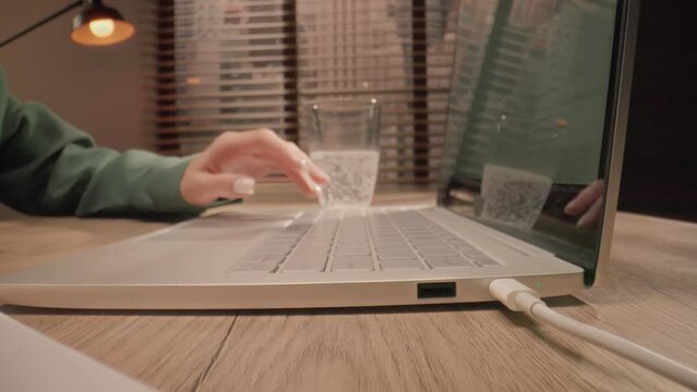 Close-up shooting. Camera slowly moving towards objects at table surface. Person's hand makes notes with pencil, working at computer on desk, typing on a laptop. Concept of online studying.
