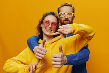 Obraz premium Man and woman couple smiling cheerfully and crooked with glasses, on yellow background, symbols signs and hand gestures, family shoot, newlyweds.