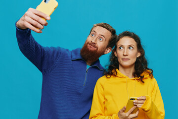 Woman and man funny couple with phones in hand taking selfies crooked smile fun, on blue...