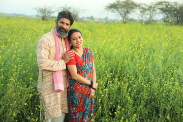 Happy Indian farmers standing in the mustard field and enjoying the benefits from the flourished rural mustard crop. husband and wife are happy to see the crops.