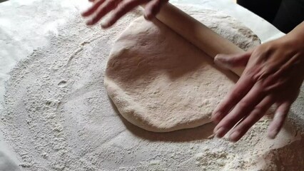 Women's hands roll out the dough with a wooden rolling pin on the kitchen table. The process of cooking at home. Top view.