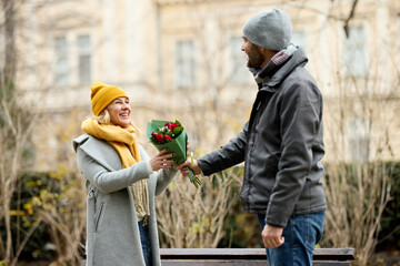 Mid adult couple relaxing in the park with man offering bouquet of flowers