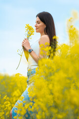 Happy beautiful woman walking on the field with yellow flowers