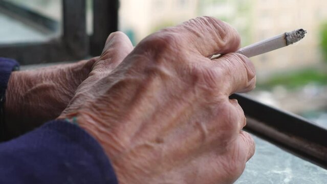 close-up hand of an elderly man holding a smoking cigarette, a pensioner smokes a cigarette while on the balcony