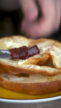 A person spreads strawberry jam on a buttered croissant