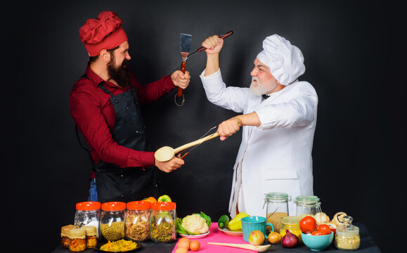 Two chefs fighting with kitchen utensils. Professional culinary. Chefs in uniform compete in culinary show. Cooking challenge. Culinary battle. Kitchen rules. Two restaurant chef. Competition of chef.