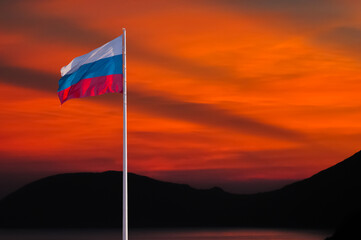 Waving Russian flag against a red sky at sunset with clouds and empty space for text. Room for text. State flag of the Russian Federation. Dark red background.