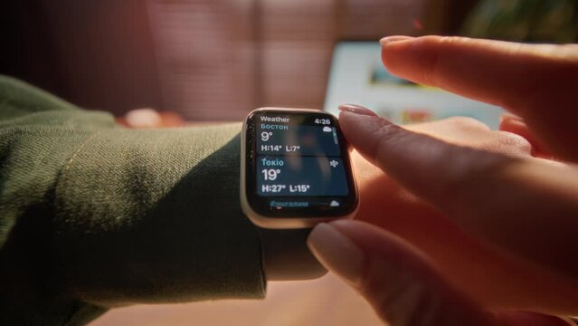Portrait of close up female hands setting smart watch with weather icons in different cities on screen. Woman at workplace checking serviceability of modern digital smart watch.