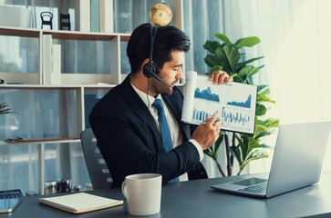 Business man wearing headphone present financial data or BI paper via laptop during online meeting....