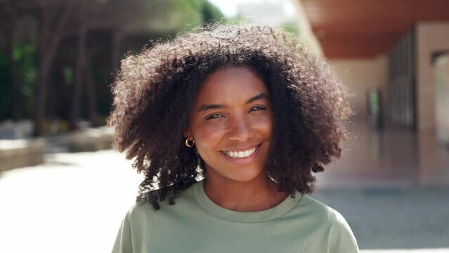Young happy cute pretty young beautiful African American woman model with flying curly hair enjoying new hairstyle advertising afro hair care product in city street outdoors on sunny day, portrait.