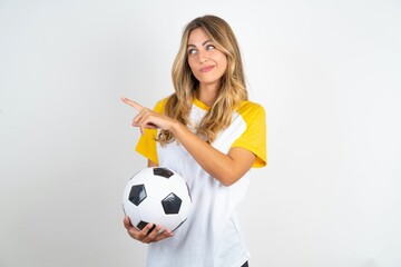 Young beautiful woman wearing football T-shirt over white background points at copy space and advertises something, advices best price.