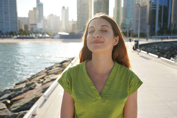 Portrait of beautiful young Brazilian woman with closed eyes enjoying sun on city promenade at sunset
