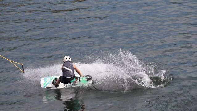 Wakeboarder ride on cable wakeboard in park, outdoor extreme on water, surfing athlete on water, young man riding a wakeboard on the river, A man practicing cable wakeboarding on a pond in a wake park