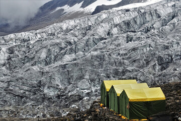 Vibrant green and yellow expedition tents stand against the stunning Manaslu Glaciers at the renowned Manaslu Base Camp in the Nepalese Himalayas.