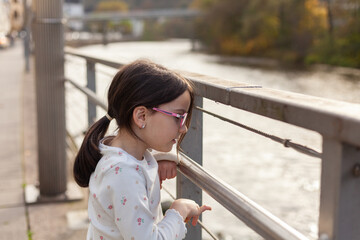 little girl with glasses on the bridge over the river, autumn day
