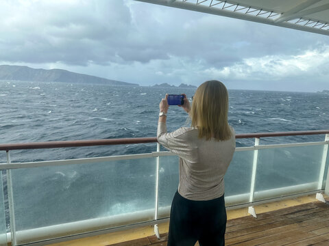 A woman taking pictures of Cape Horn from a cruise ship balcony