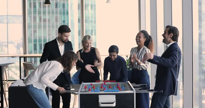 Joyful excited employee beating office friend in tabletop football, laughing, giving high five. Couple of cheerful colleagues competing in table soccer, having fun, getting diverse team fan support