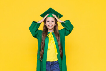 A child in a graduate costume. The school girl rejoices at the end of the year. Children's education. A little girl smiles on a yellow isolated background.