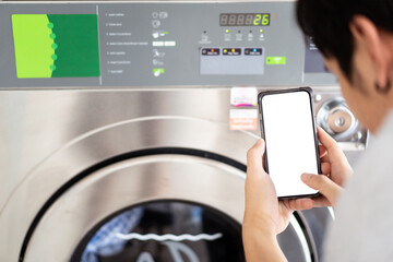 Empty white screen smartphone mockup isolated with clipping path. Asian man using an application in smartphone to pay a service charge and operating the vending washing machine.