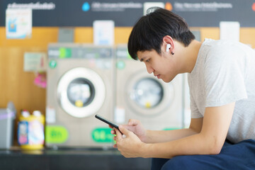 Asian man using smartphone for social networking or chatting with a friends while waiting for...