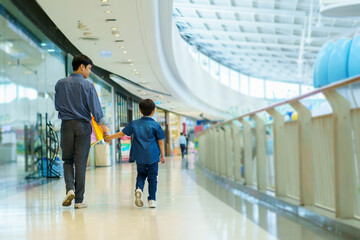 Happy cheerful Asian man and son walking tougher in the department or grocery store, man taking his son to shop a clothing and toys in the department store or mall.