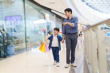 Fototapeta premium Happy cheerful Asian man and son walking tougher in the department or grocery store, man taking his son to shop a clothing and toys in the department store or mall.