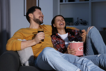 Couple watching comedy via TV and laughing at home in evening