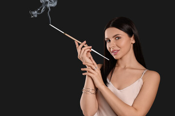 Woman using long cigarette holder for smoking on black background, space for text