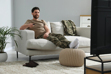 Happy soldier watching TV on sofa in living room. Military service