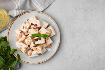 Pieces of delicious nutty nougat, mint and honey on light gray table, flat lay. Space for text