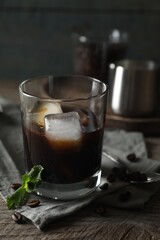Glass of delicious iced coffee, mint and beans on wooden table