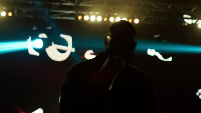 African-American Black rap artist performing his gig on a stage of a large venue, surrounded by bright flashig lights