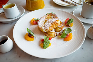 French toast with maple syrap, rasp berry sauce and fruits on a white plate.