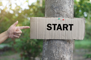 Finger points to paper card with word START, stick on trunk of tree. Concept, giving for direction, sign and notice, Teaching aids, vocabulary on word card. Start point.  