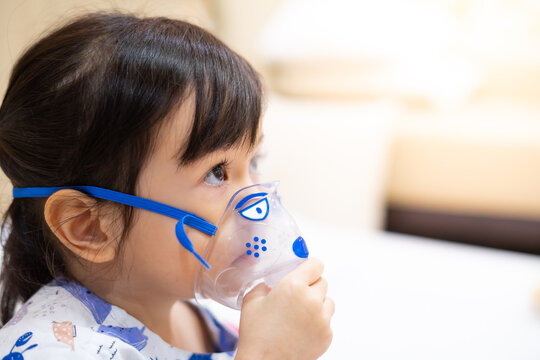Little asian girl sick making inhalation with nebulizer to reduce coughing and sputum in the neck , lying in bed at hospital, child taking medication while breathing in through face mask