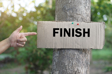 Finger points to paper card with word FINISH, stick on trunk of tree. Concept, giving for direction, sign and notice, Teaching aids, vocabulary on word card. Finish point.                       