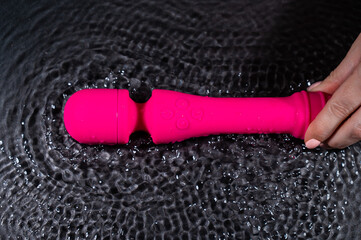 A woman holds a pink dildo in the water. Sex toy on a black background.
