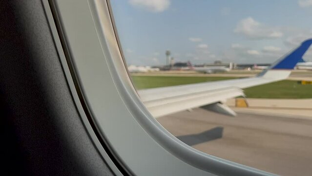 Airplane taxis down the runway, waiting in line for takeoff. Passenger point of view, looking through airplane window. Blurred motion of airport tarmac.