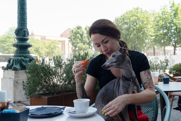 Young woman with her dog sitting in street friendly cafeteria and drink coffee.
