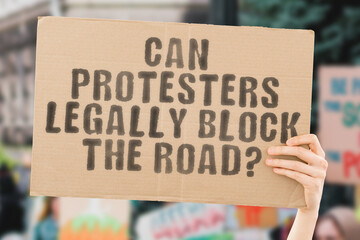 A thought-provoking image of a man's hand holding a banner with the text 'Can protestors legally block the road?' Perfect for showcasing support or protest