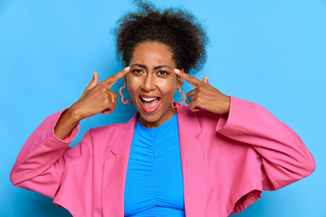Naklejka premium Portrait of beautiful black girl against blue background, having good time in studio, pressing fingers to her head and smiles, delight concept, copy space