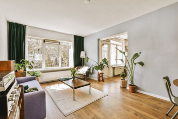 a living room with wood flooring and green drapes on the window sies, some plants in pots