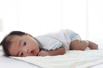 Cute happy newborn infant baby boy lying down on white bed in bedroom, lovely child sleeping on stomach, nursery for kid children family concept.