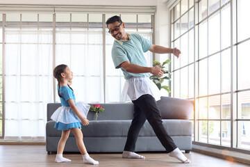 Fototapeta na wymiar Cute little girl with young cheerful handsome dad wearing beautiful skirt and dancing together, dad trying to train his daughter to dance ballet, Happy family spending time together. Happy Father Day.
