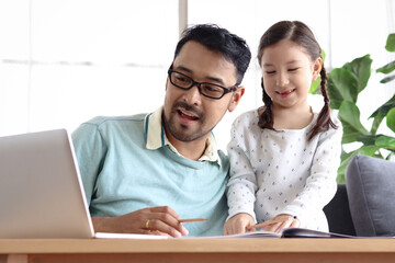 Father teaches cute girl daughter to do school homework, using laptop computer for e-learning study at home, happy family dad and kid spending time together for education and searching Internet.