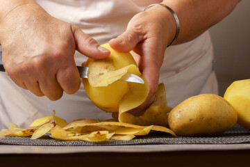 close-up of a woman's hands in a white apron peeling potatoes with a knife.