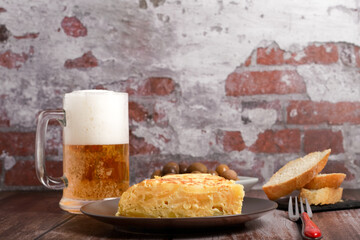 typical spanish potato omelette freshly made on a wooden table with a fresh pitcher of beer,...