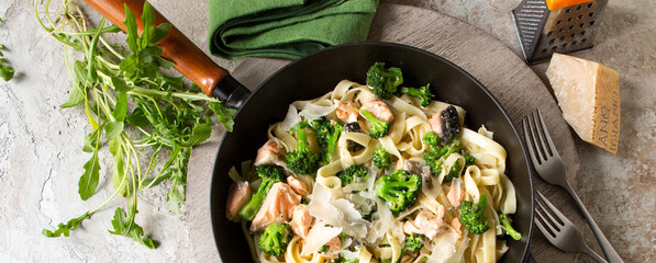 frying pan with homemade tagliatelle pasta with salmon and broccoli on the table